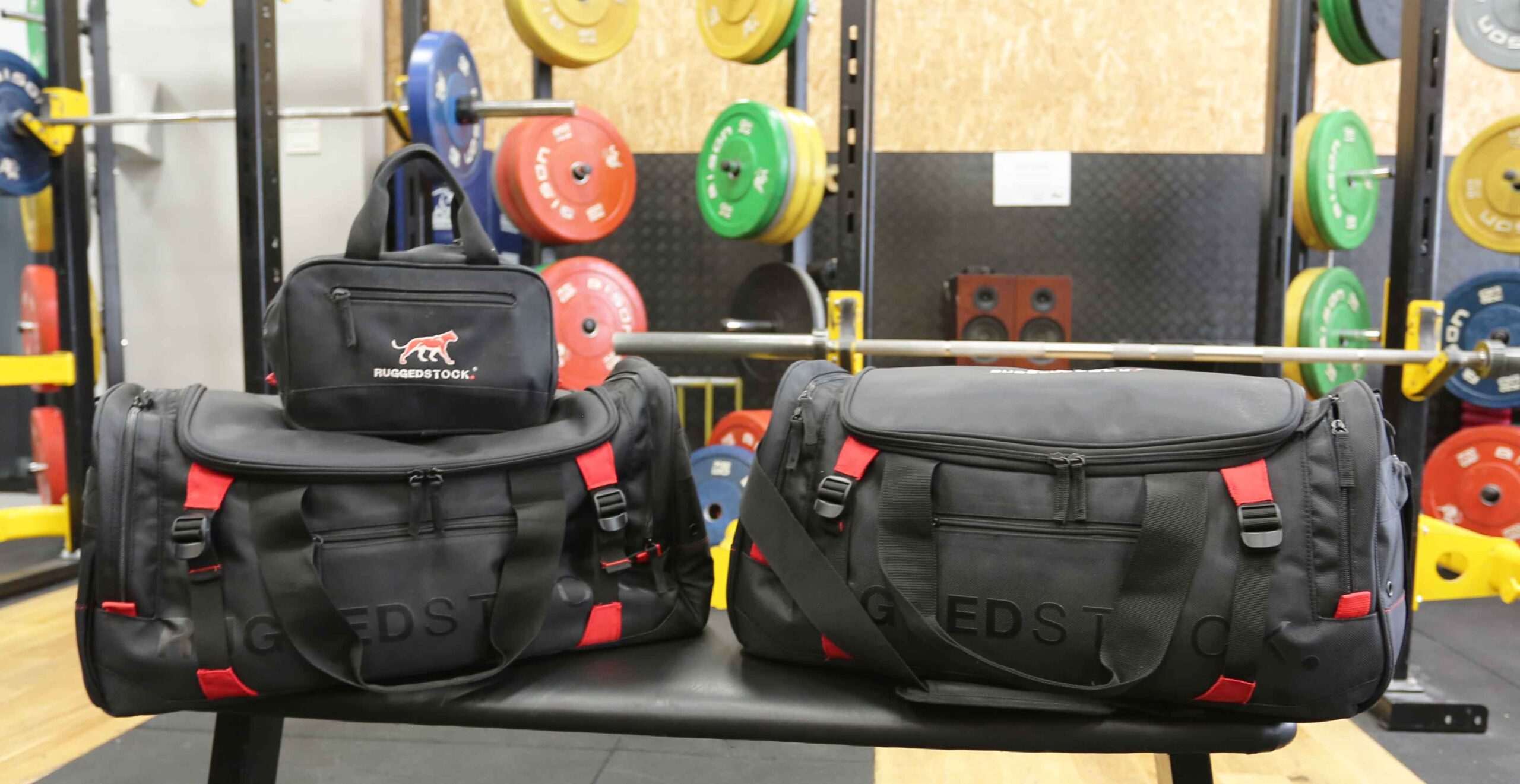 Two Ruggedstock duffle bags and a wash bag on weight training bench at a gym